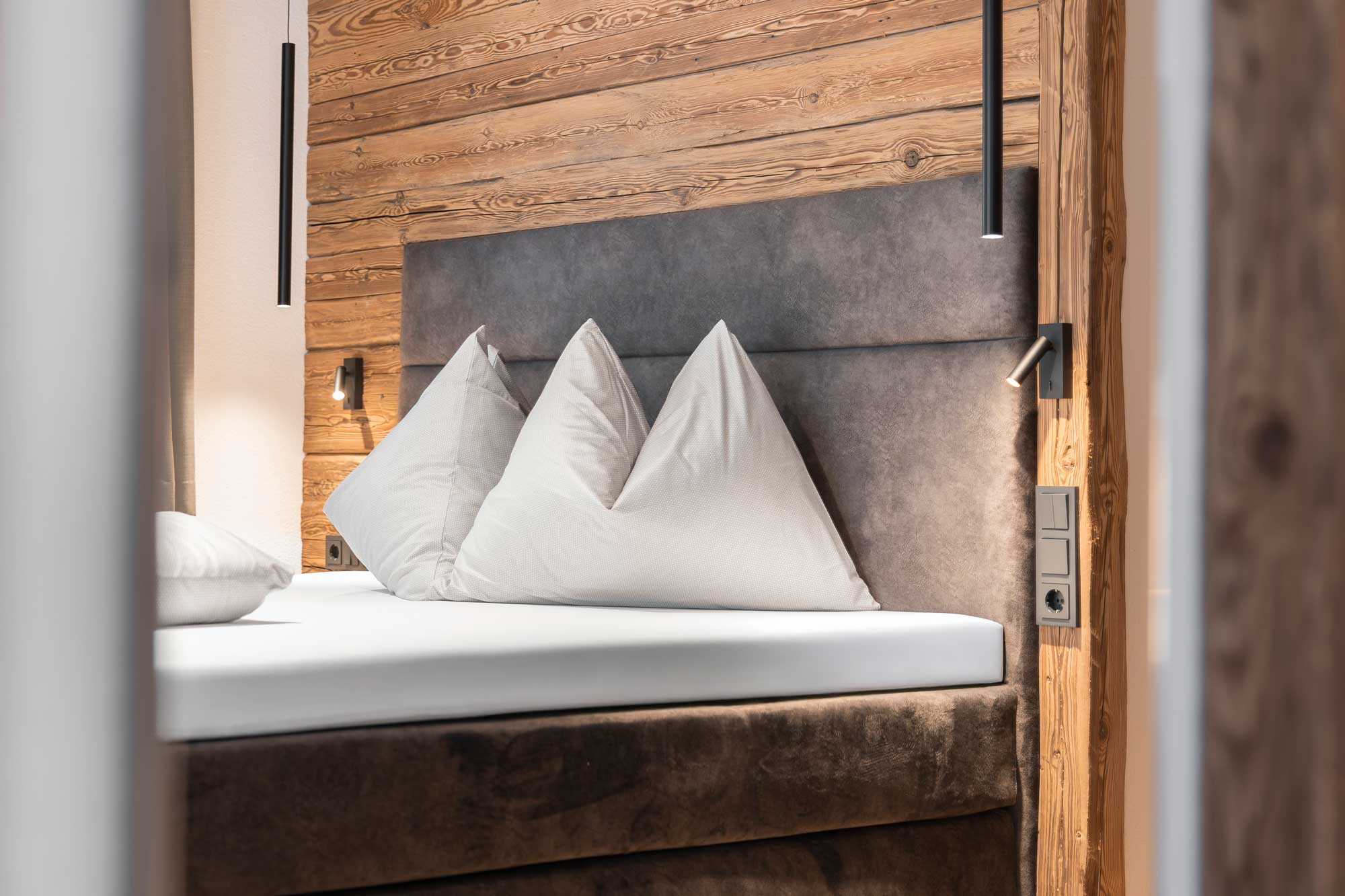 Modern bed with three large white pillows against a wooden wall in a cozy bedroom.