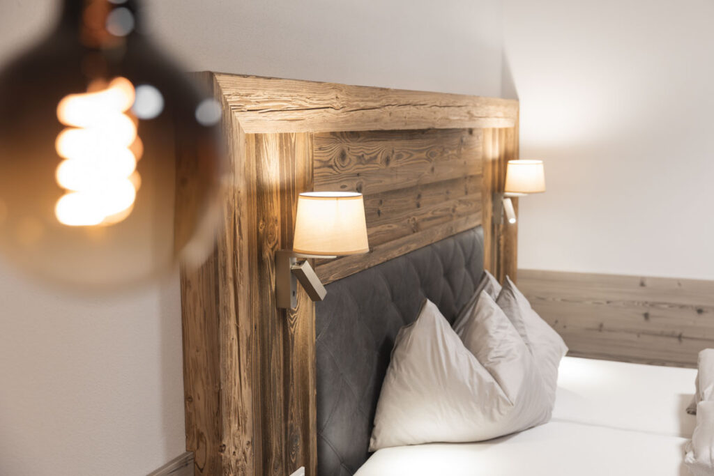 Close-up of a cozy bed with wooden headboard, two pillows, and wall-mounted lamps.